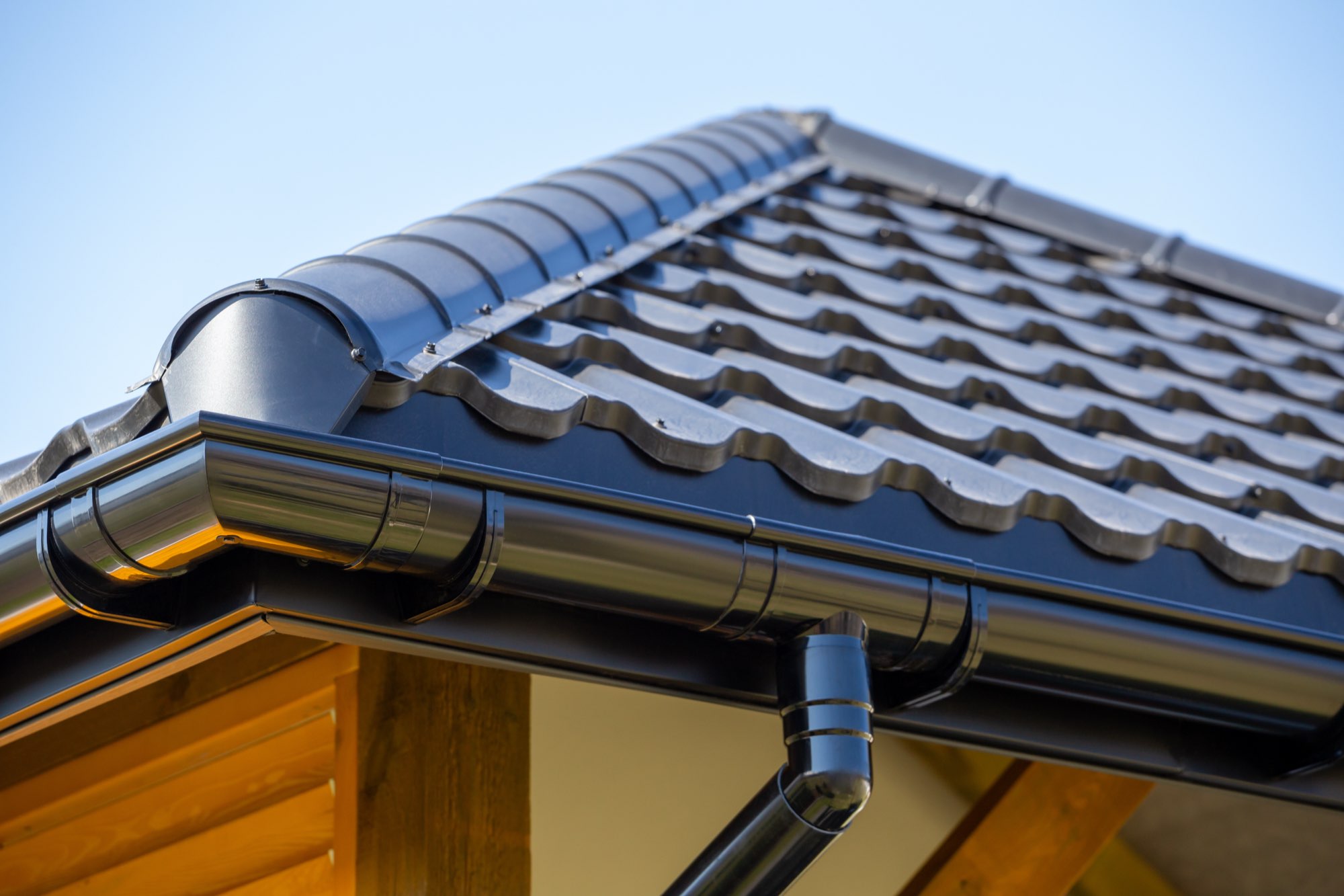Black seamless gutter and downspout installed along a dark tile roofline