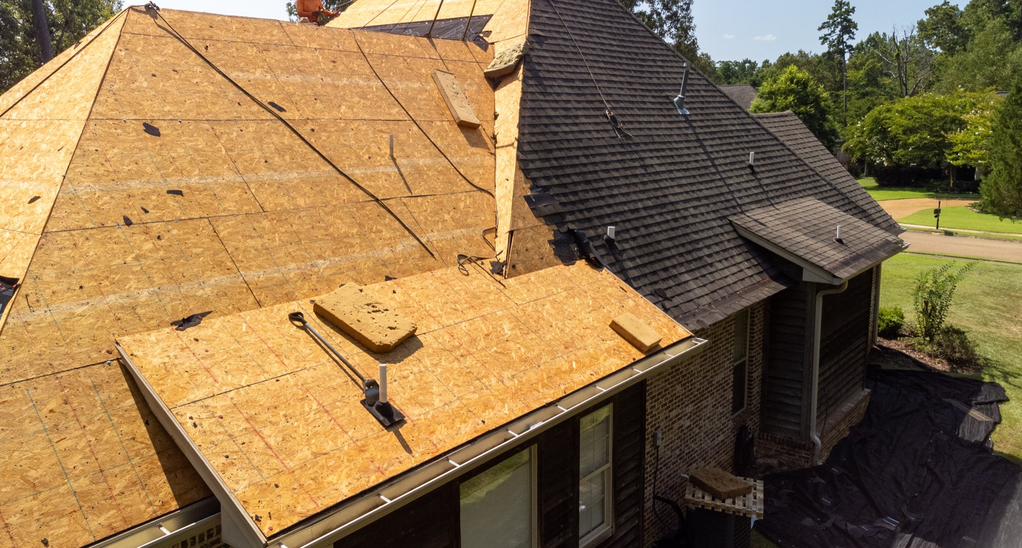 Fresh roof decking installed beside existing shingles during a repair