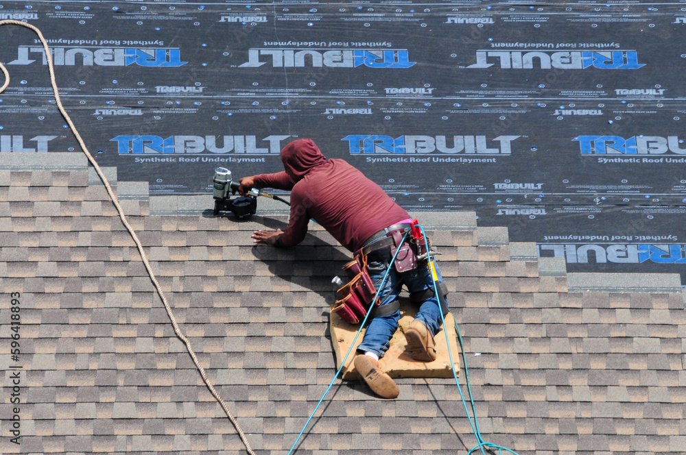Roofer installing architectural shingles over synthetic underlayment