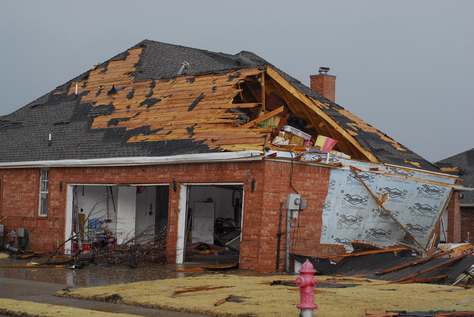 Brick home with severe storm damage to its shingle roof and gable